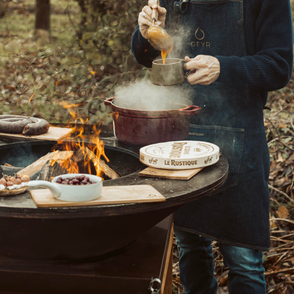 Okrągła płyta grillowa paleniska OFYR Classic 100 ze stali Corten z mięsem i warzywami w różnych strefach temperatury